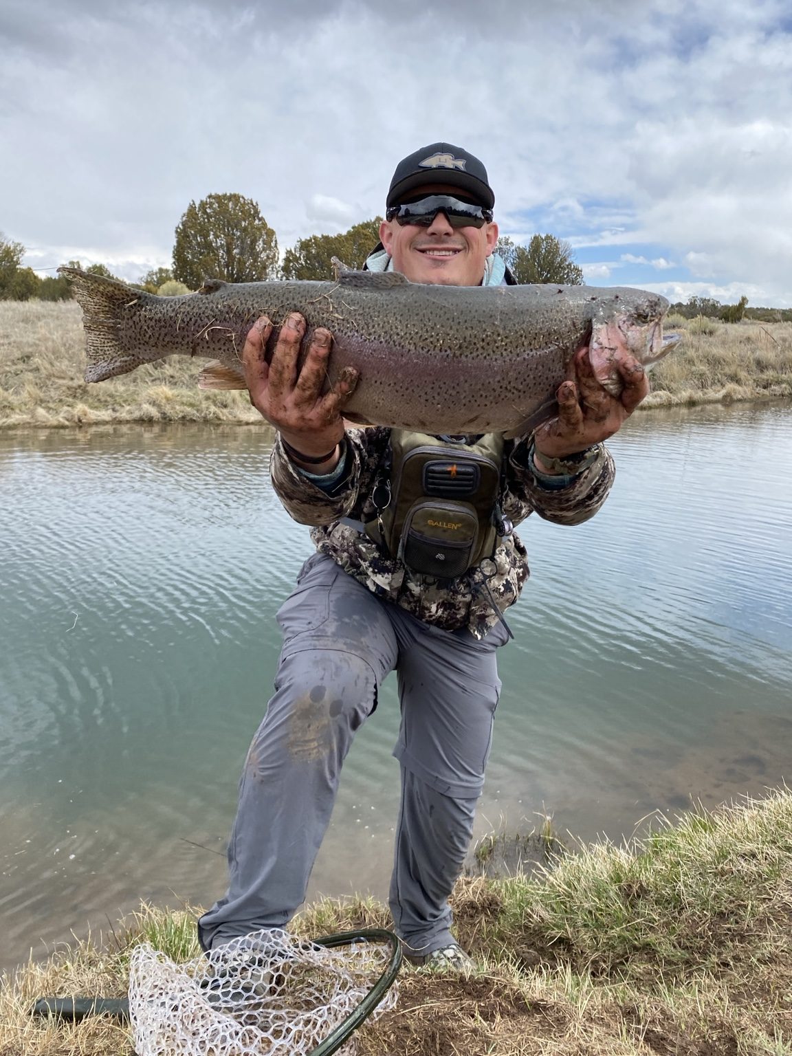 Angler holding a large rainbow trout beside the water